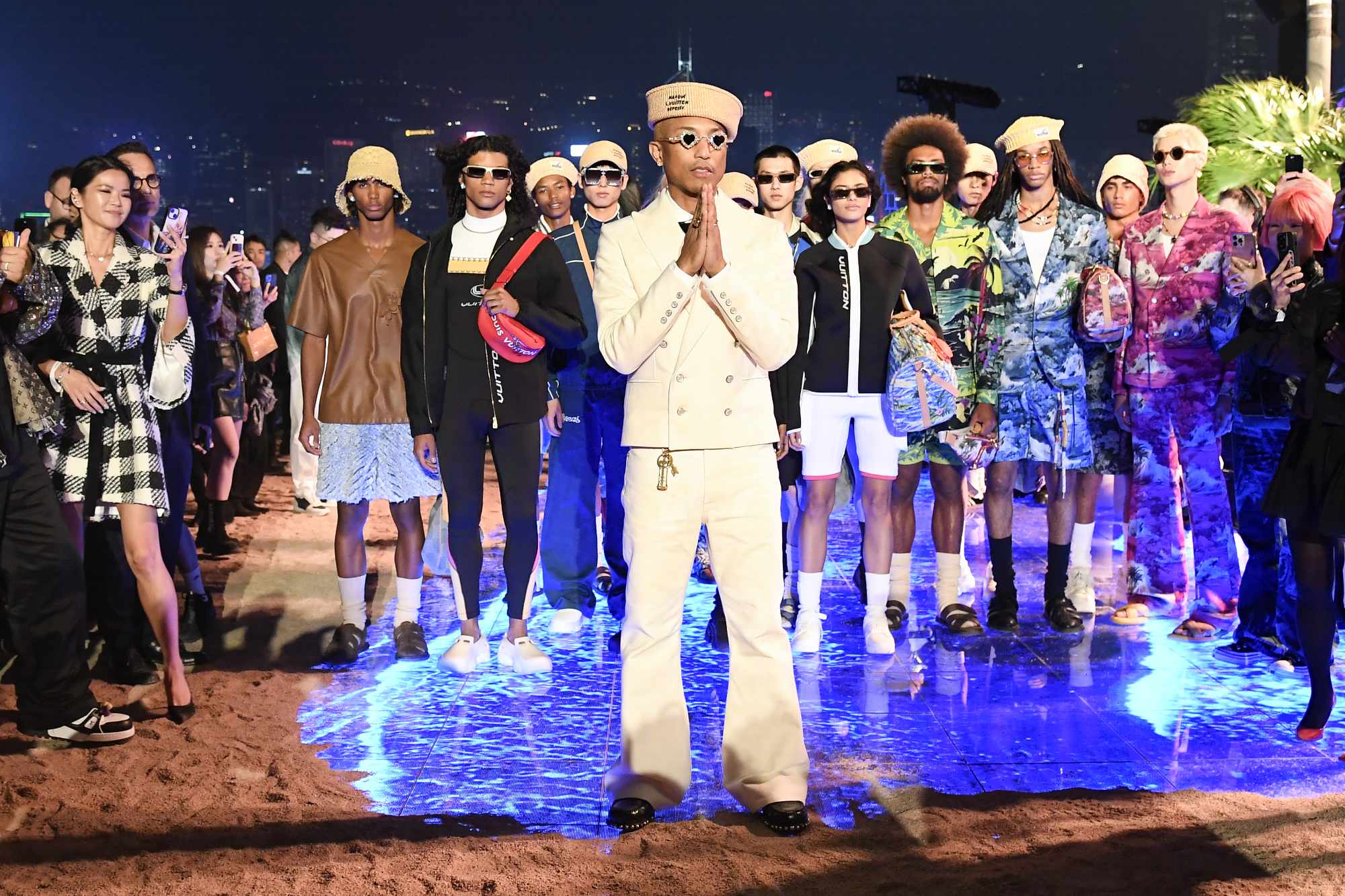 Pharrell Williams wearing a white suit and Tiffany sunglasses stands in front of models on the Louis Vuitton Pre-Fall 2024 runway in Hong Kong