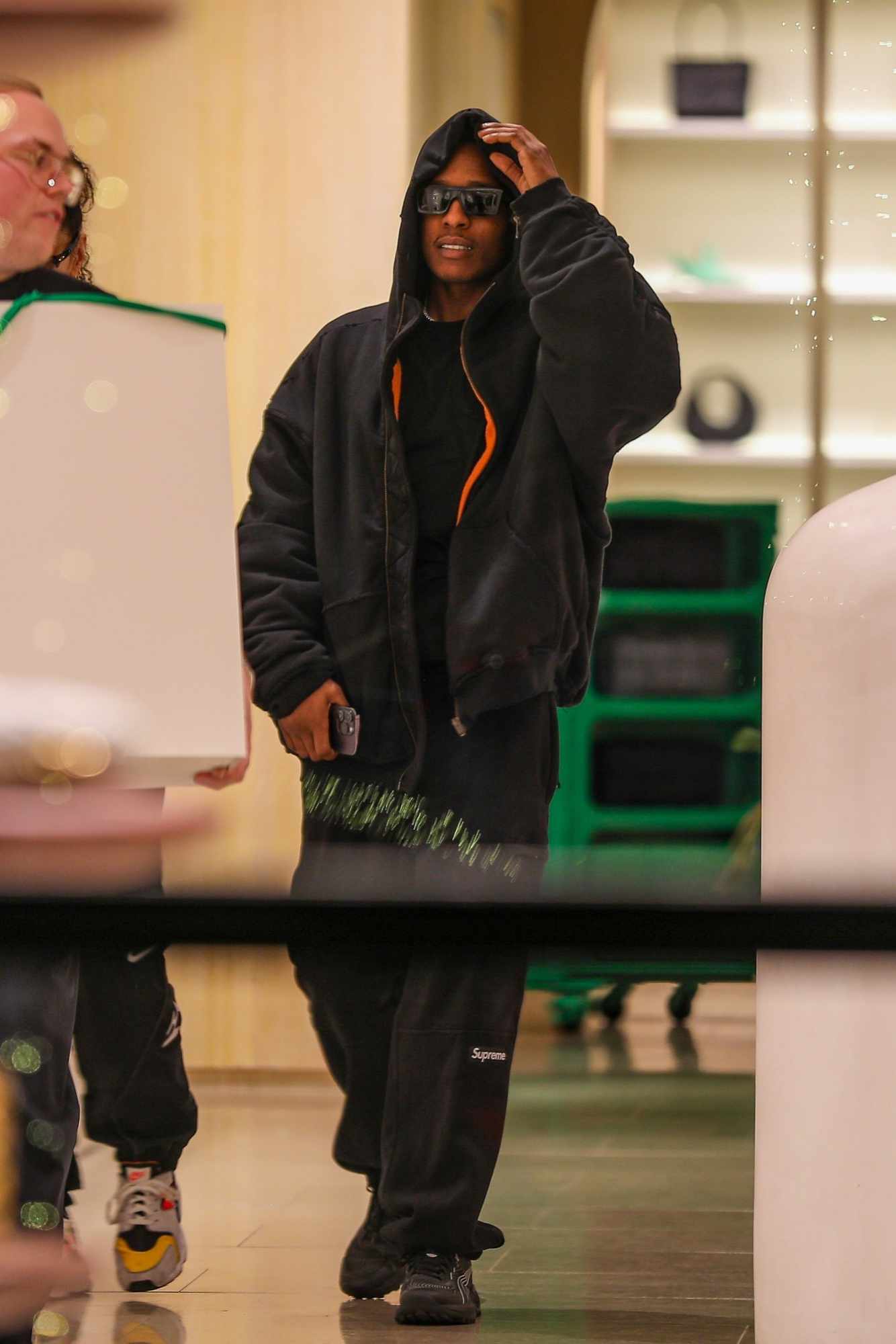 Asap Rocky wears black sunglasses, a leather jacket, Supreme sweatpants, and PUMA sneakers at the Bottega Veneta store in los Angeles