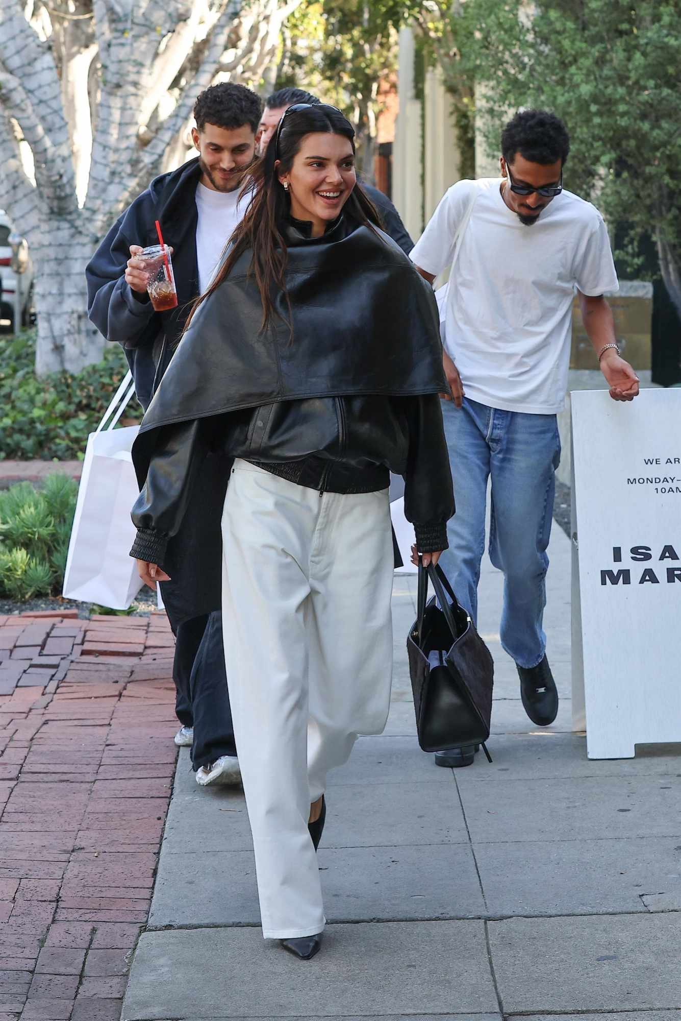 Kendall Jenner wears Phoebe Philo's black leather bomber and cape with wide white pants in December 2023