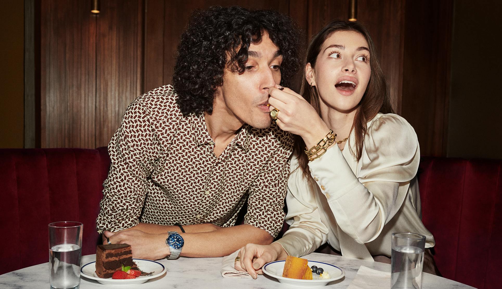 Woman feeding man food at bar while wearing fossil accessories