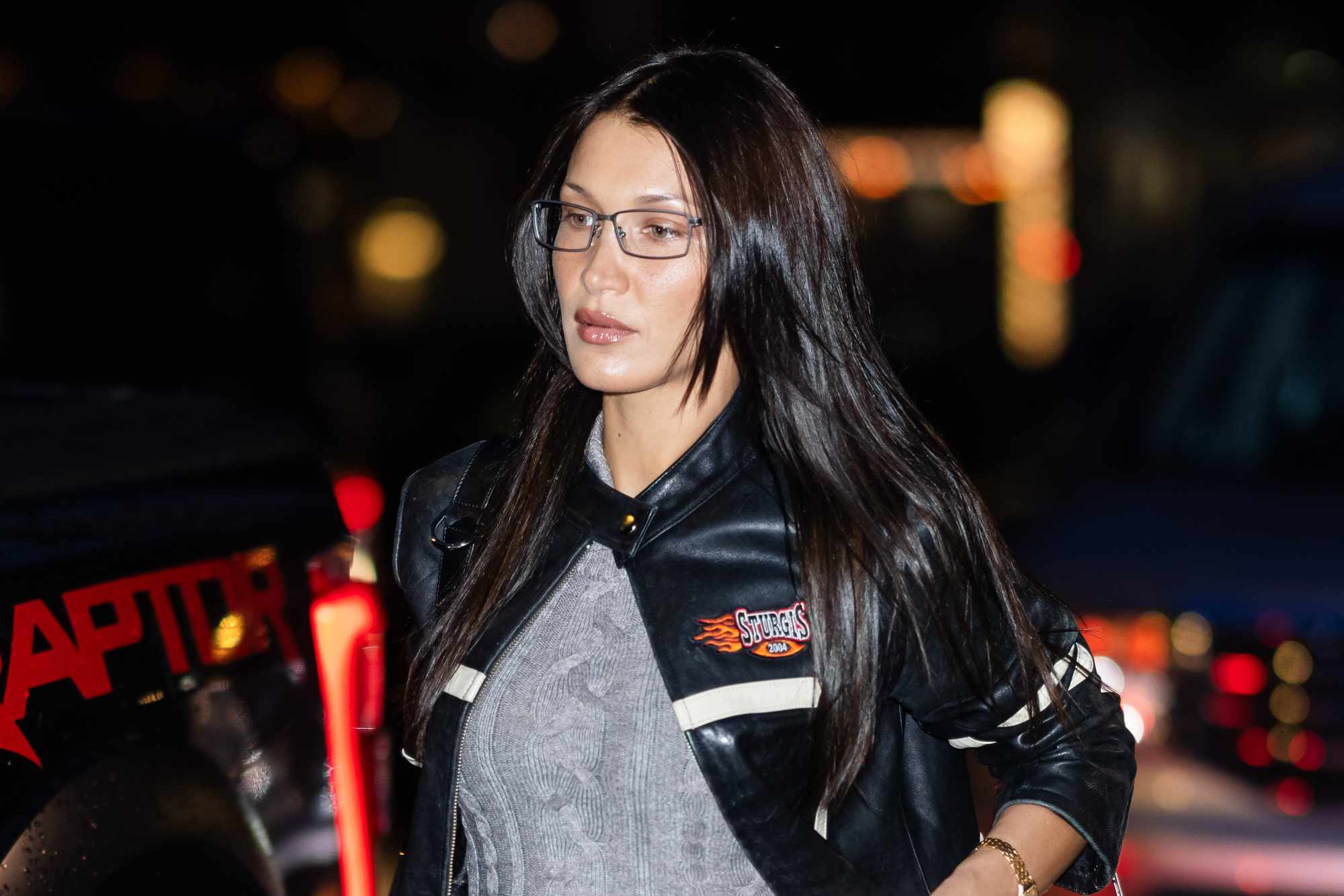 Bella Hadid wears thin-frame glasses, a black leather racing jacket, and teal knit sweater in New York on December 17