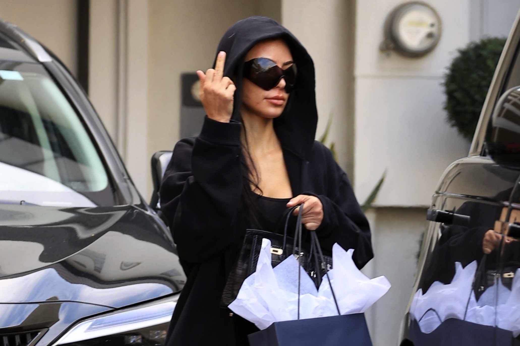 Kim Kardashian wears Balenciaga sunglasses & a black sweatsuit while giving paparazzi the middle finger