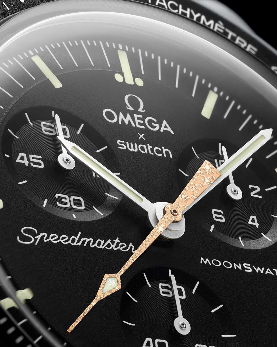 A close-up photo of OMEGA & Swatch's cold moon-inspired Moonswatch watch collab, showing a black watch face and gold hands with a snowflake pattern