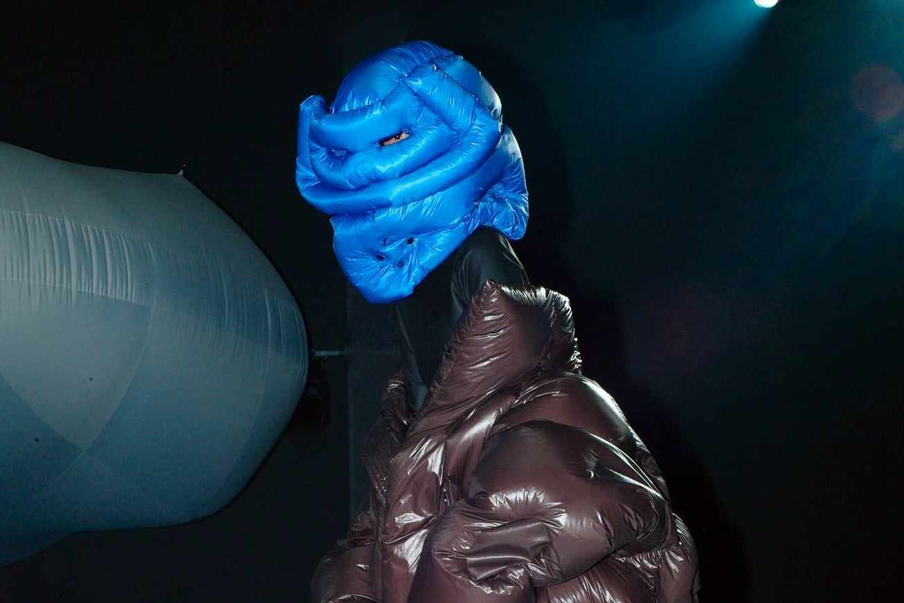 A model wears a blue Dingyun Zhang x Moncler puffer hat & black puffer coat