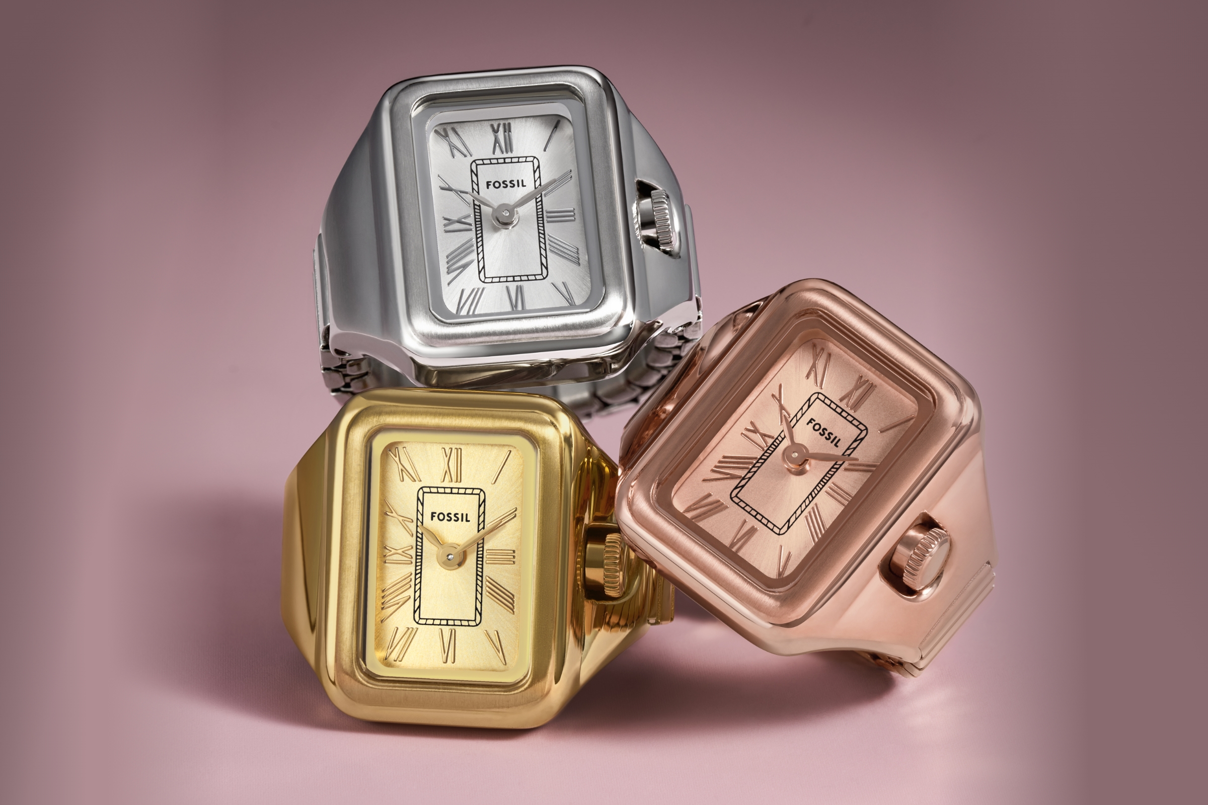 Fossil Raquel Watch Rings in gold, rose gold, and silver set against pink background