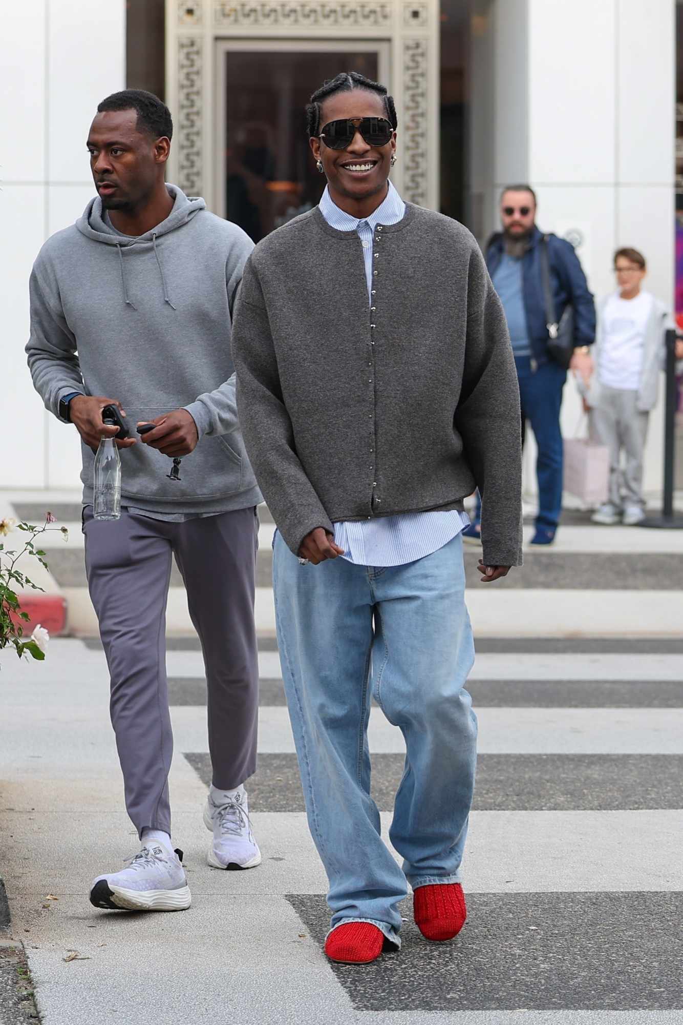 A$AP Rocky wears a grey cardigan, blue shirt, denim jeans, and red leather sock shoes