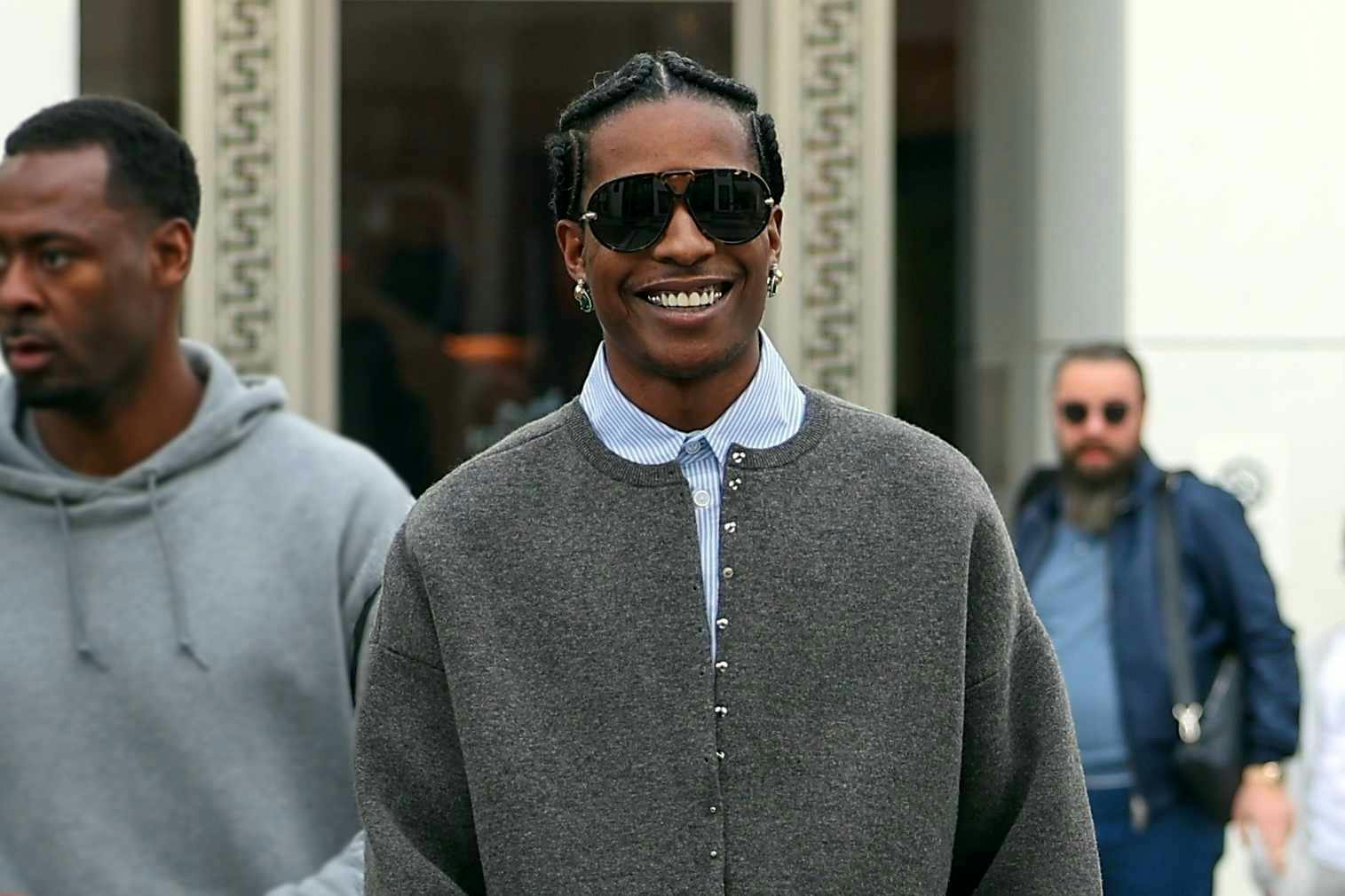 A$AP Rocky wears a grey cardigan, blue shirt, denim jeans, and red leather sock shoes