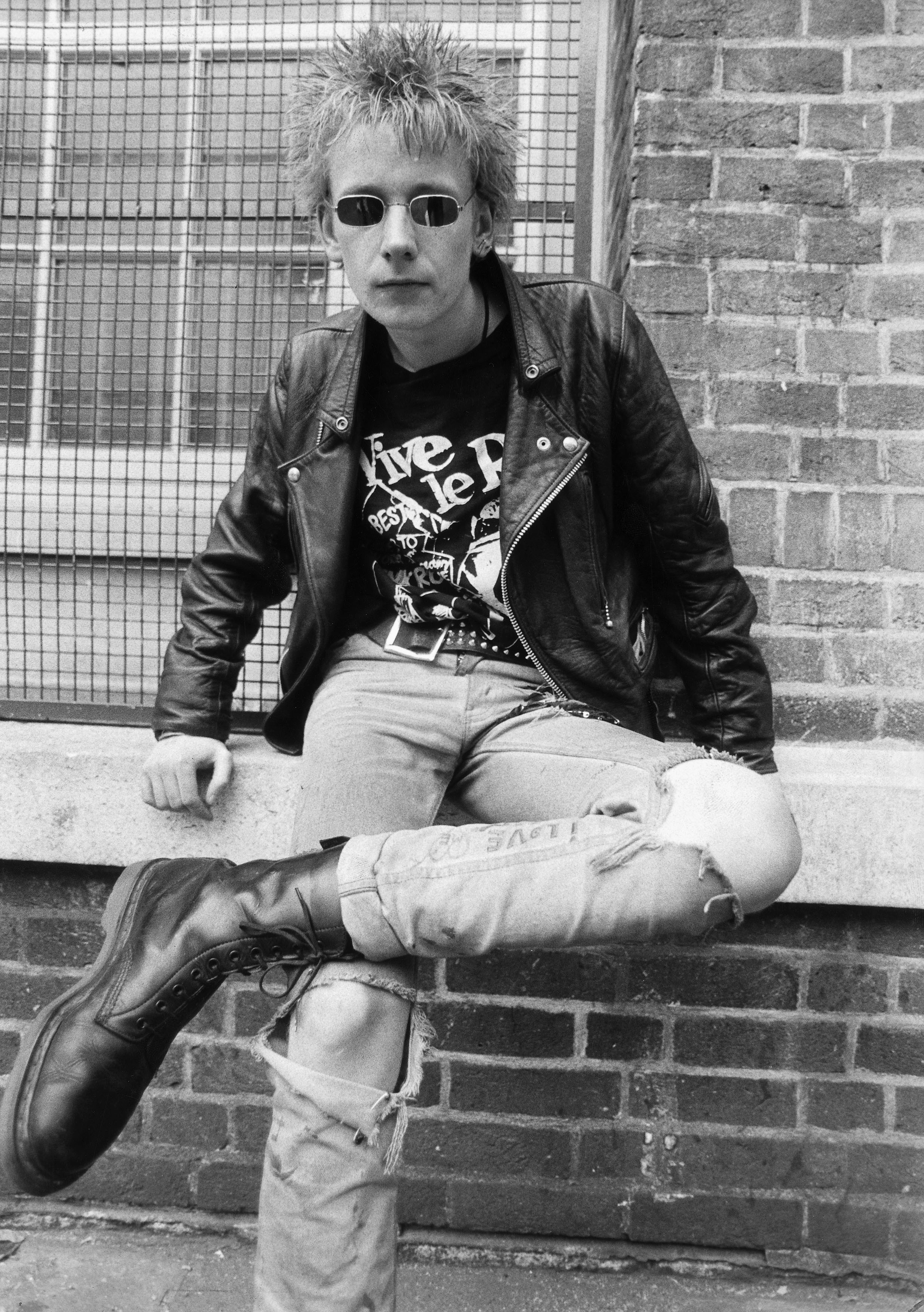 A young man wears typical punk dress: a leather jacket, torn jeans, Doc Martens boots, and a safety-pin earring, 1985.