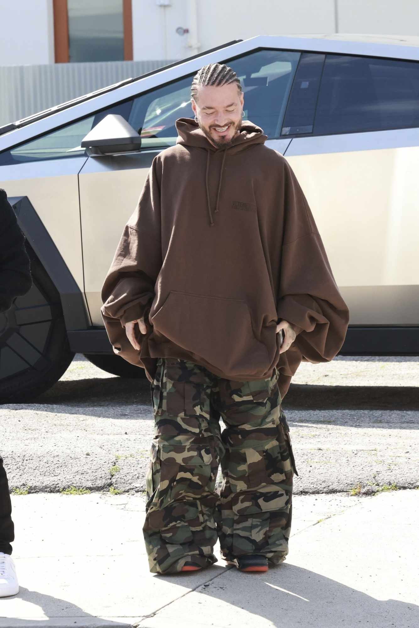 J Balvin wears a Vetements 16XL hoodie with camouflage pants next to his silver tesla cybertruck
