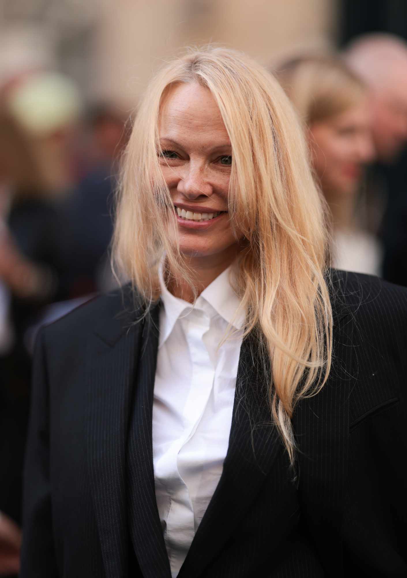 Pam Anderson wears a grey blazer and white shirt at The Row's FW24 fashion show in Paris