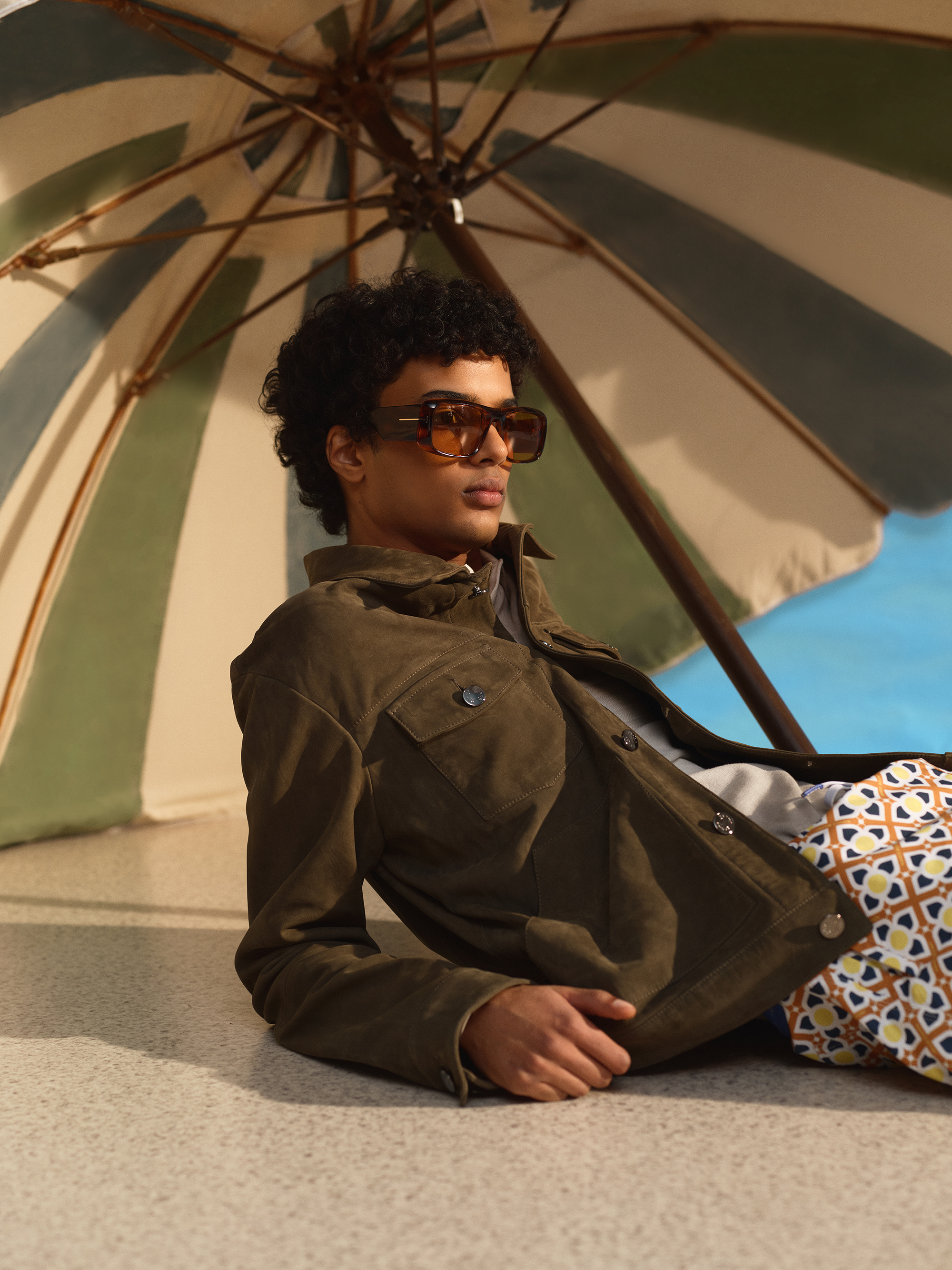 A model reclines in a khaki look under an umbrella