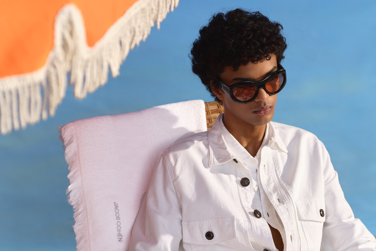 Man reclines next to parasol wearing white jacket and sunglasses