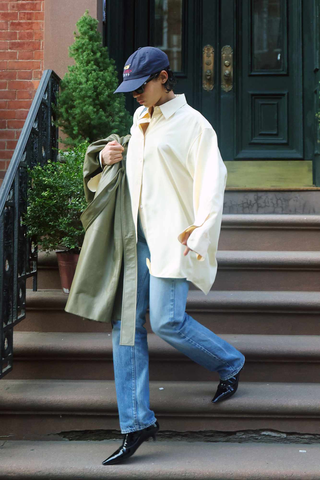 Taylor Russell wears a blue hat, oversized white shirt, washed jeans, and black heeled boots
