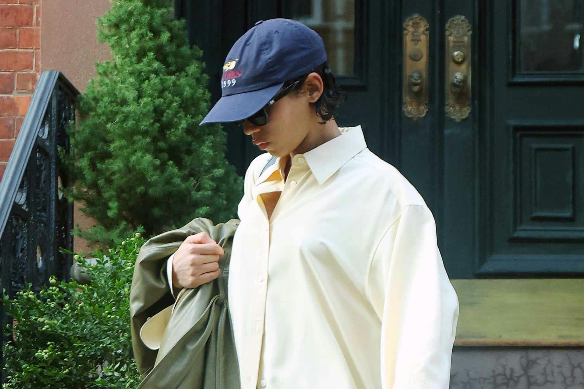 Taylor Russell wears a blue hat, oversized white shirt, washed jeans, and black heeled boots