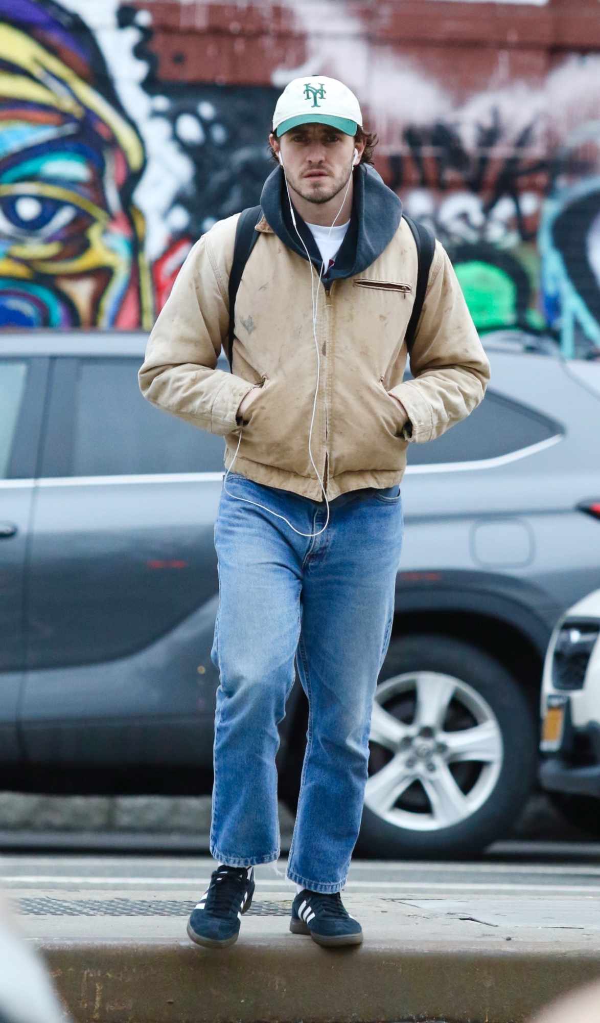 Paul Mescal wears wired earbuds, a Carhartt jacket, jeans & adidas sneakers
