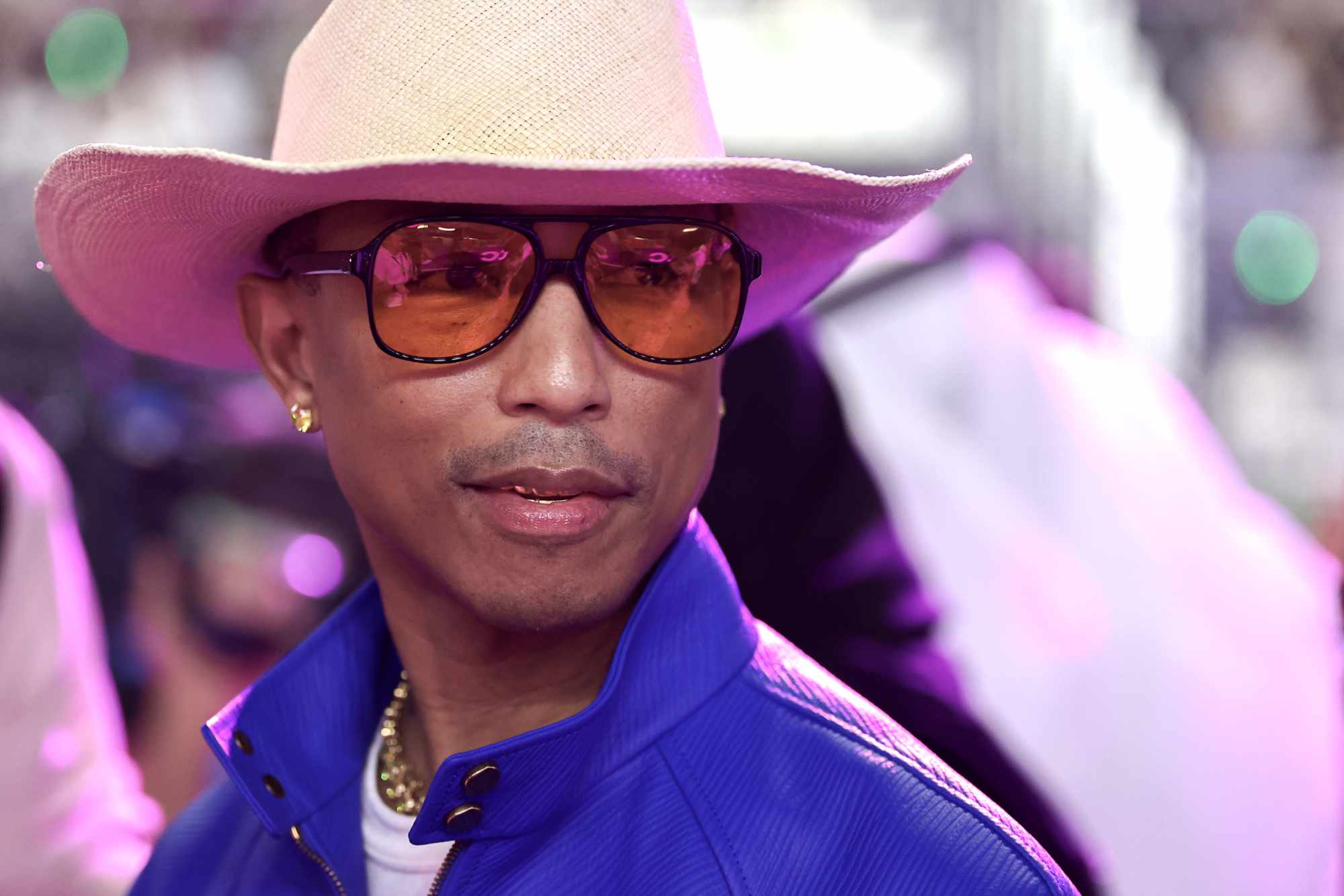 Pharrell Williams wears a white cowboy hat, yellow sunglasses, and a blue jacket at the March 9 F1 Grand Prix of Saudi Arabia