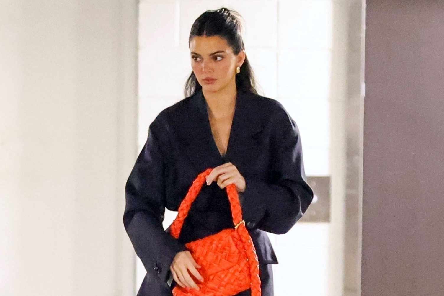 Kendall Jenner wears a navy Bottega Veneta suit with a red intrecciato woven handbag