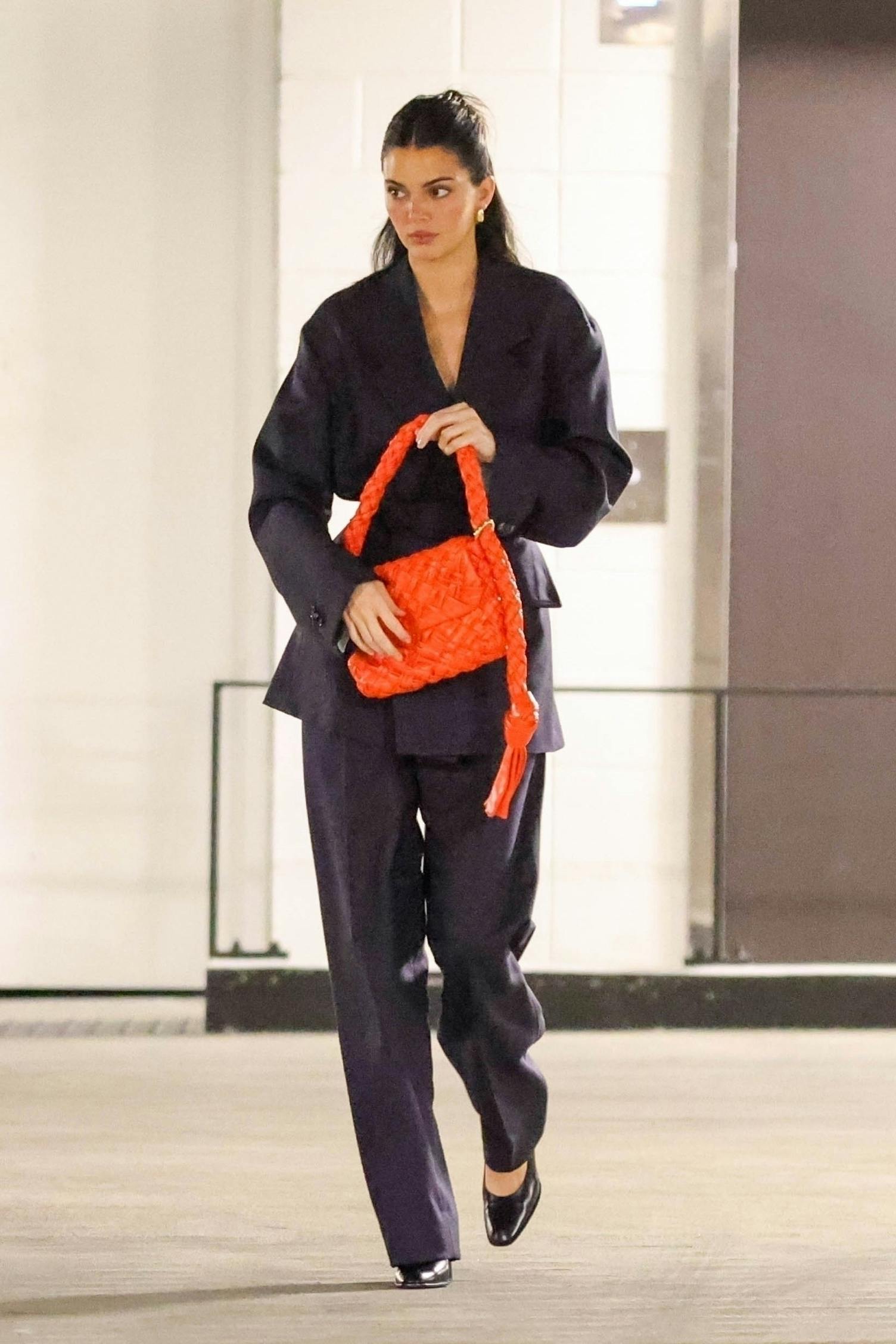 Kendall Jenner wears a navy Bottega Veneta suit with a red intrecciato woven handbag