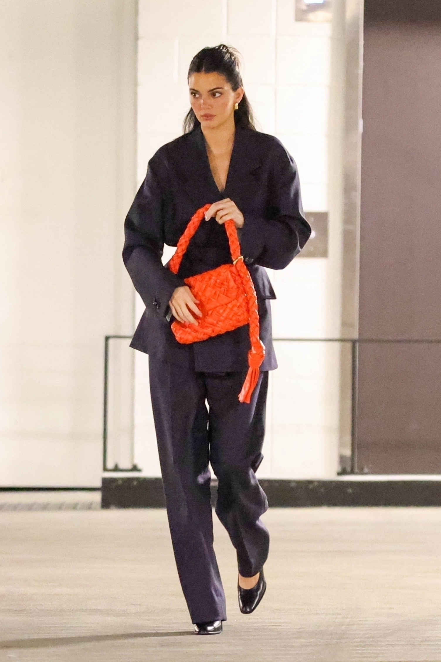 Kendall Jenner wears a navy Bottega Veneta suit with a red intrecciato woven handbag