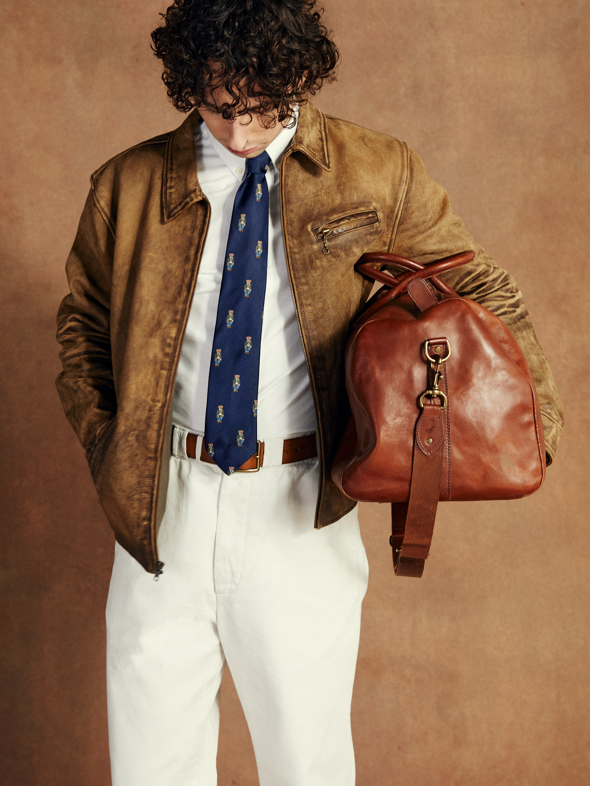 Model looks downwards carrying a suitcase and wearing a white shirt with a tie and a jacket