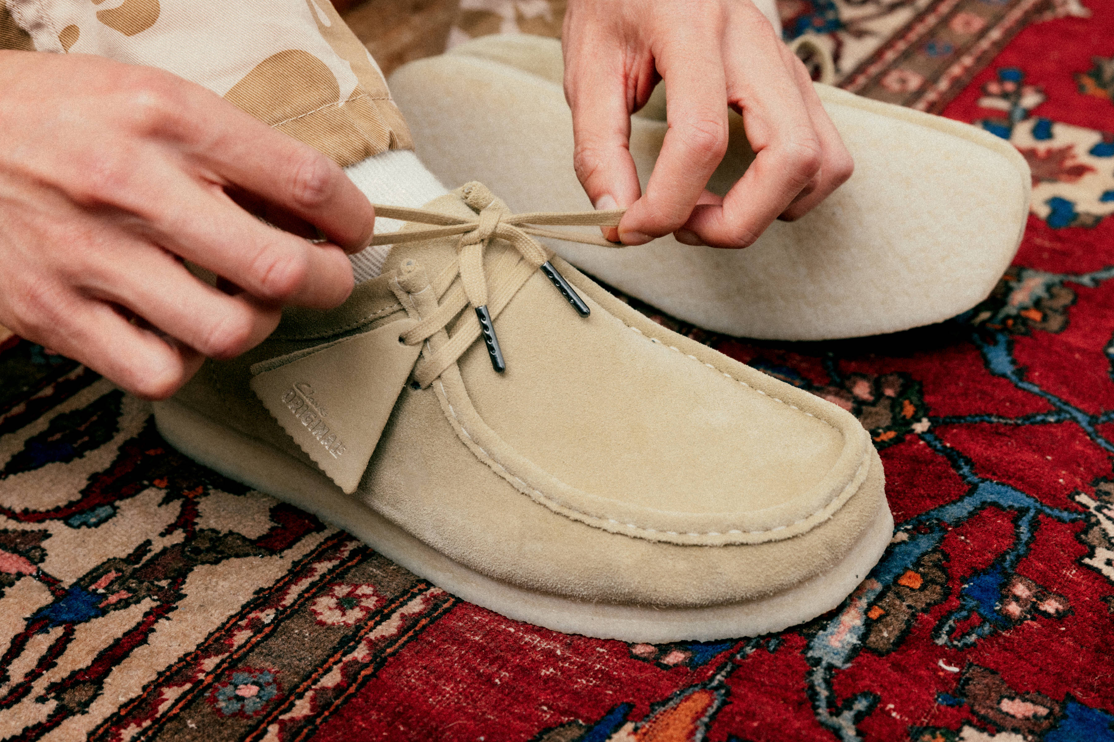 Close-up of a pair of hands tying the laces of a beige moccasin shoe