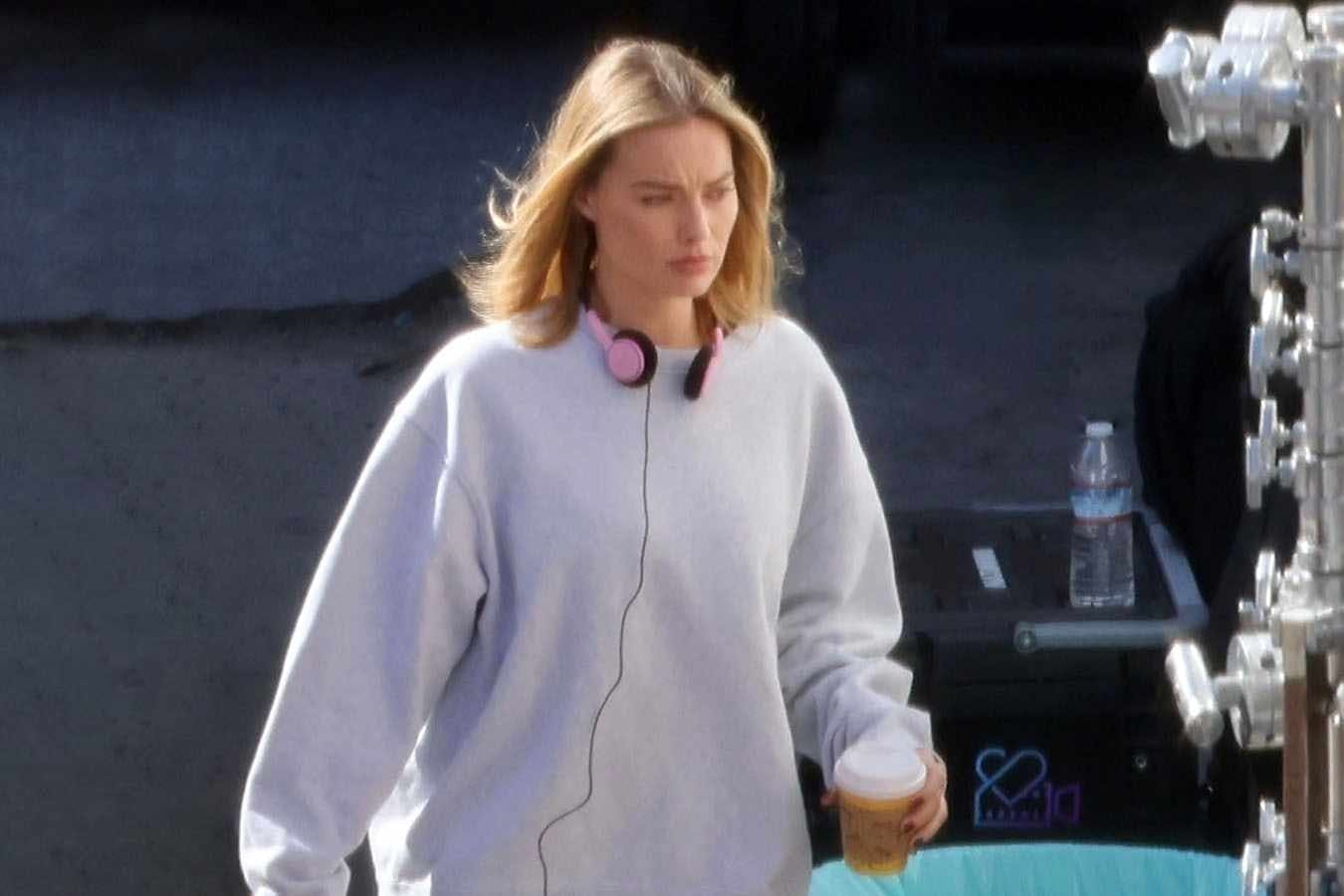 Margot Robbie wears a grey sweater, blue jeans & reebok sneakers on the set in Los Angeles for A Big, Bold, Beautiful Journey