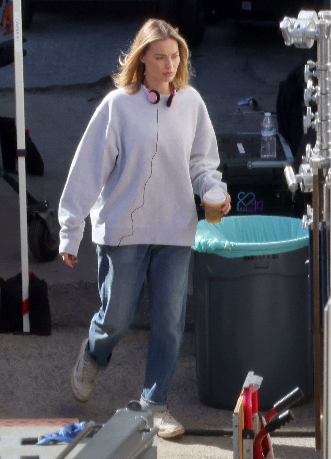 Margot Robbie wears a grey sweater, blue jeans & reebok sneakers on the set in Los Angeles for A Big, Bold, Beautiful Journey