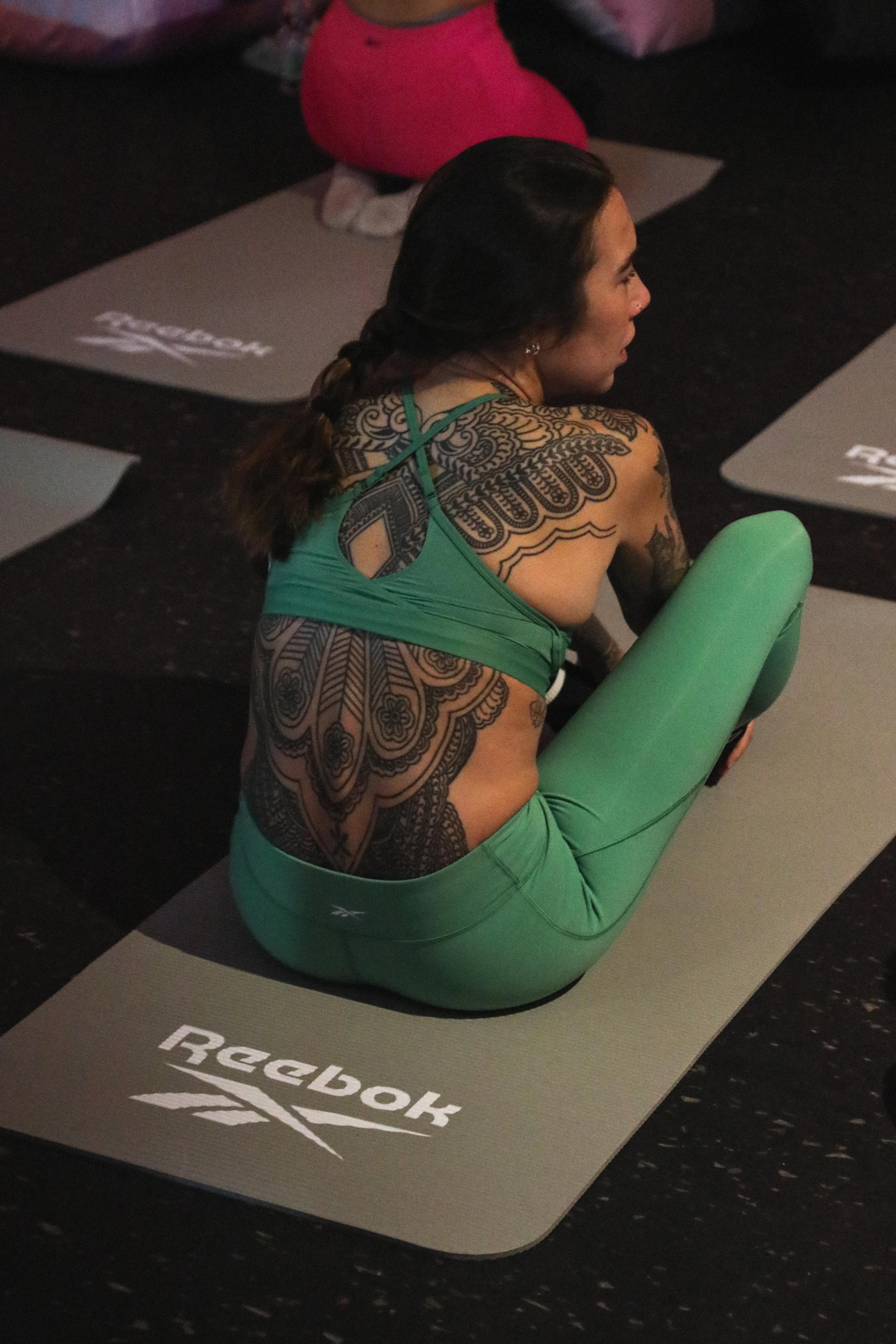 Shot from behind of a woman in green sports gear on a yoga mat