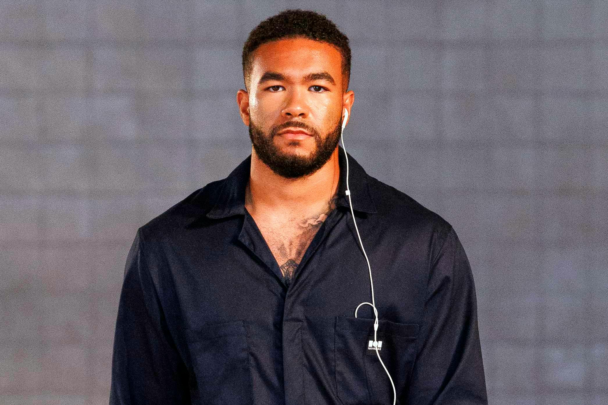 A model wears white wired earbuds on the Nahmias SS25 runway