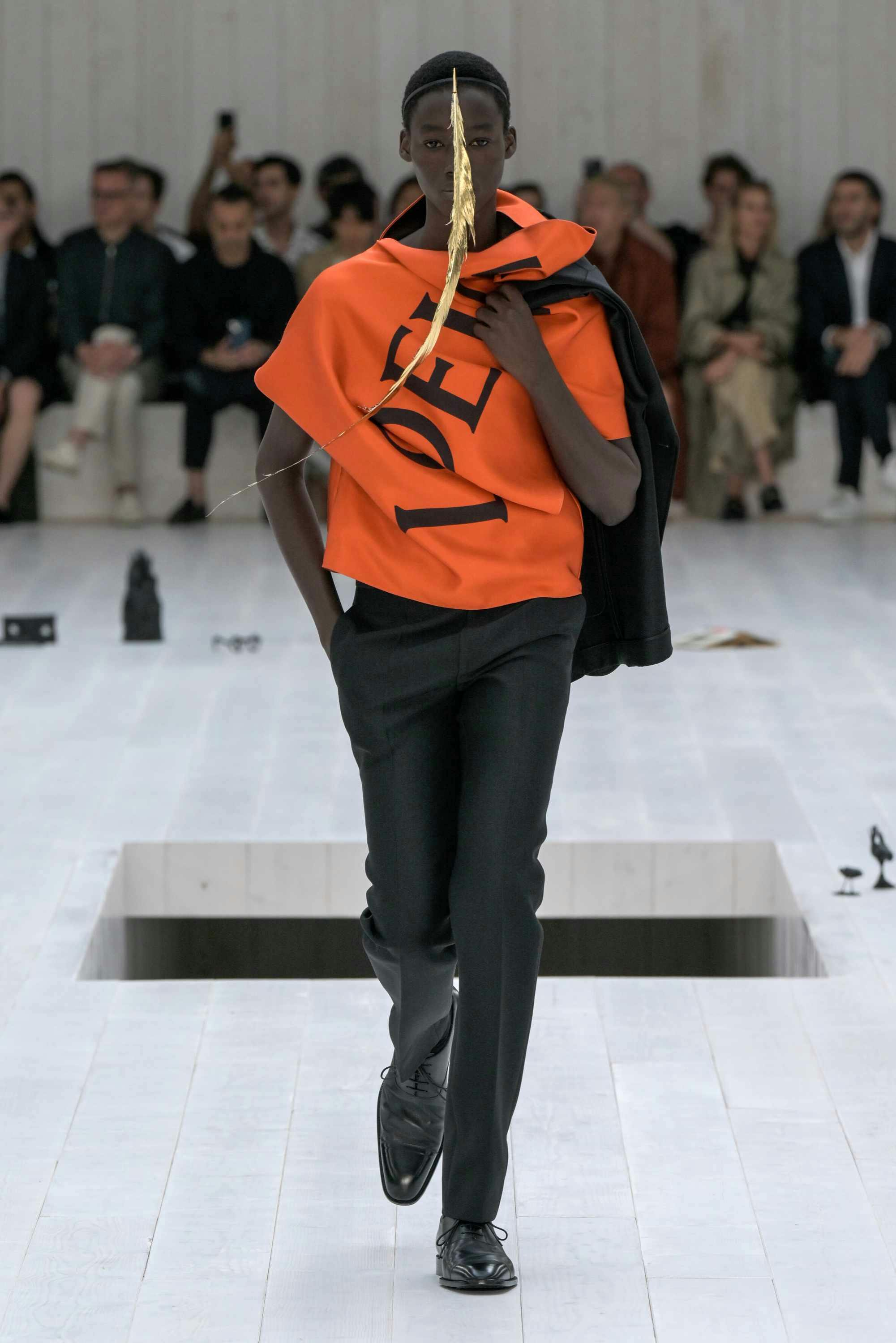 A model wears a red LOEWE shirt and black pants on the SS25 menswear runway