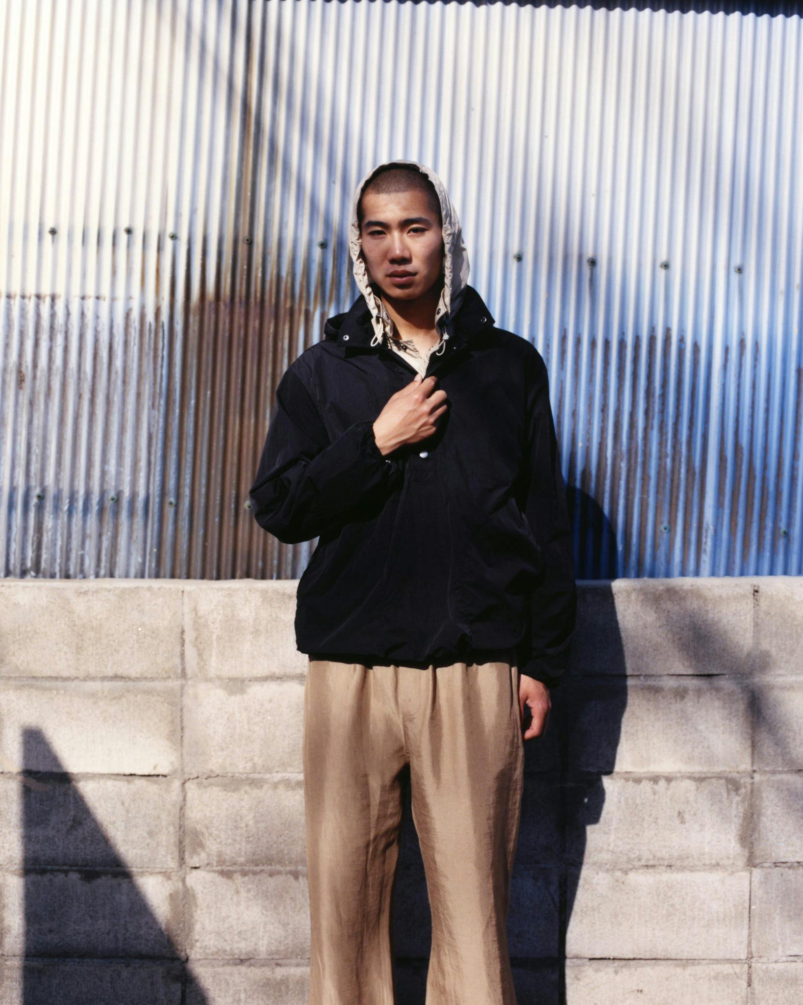 Model wearing a dark hooded jacket and loose neutral trousers