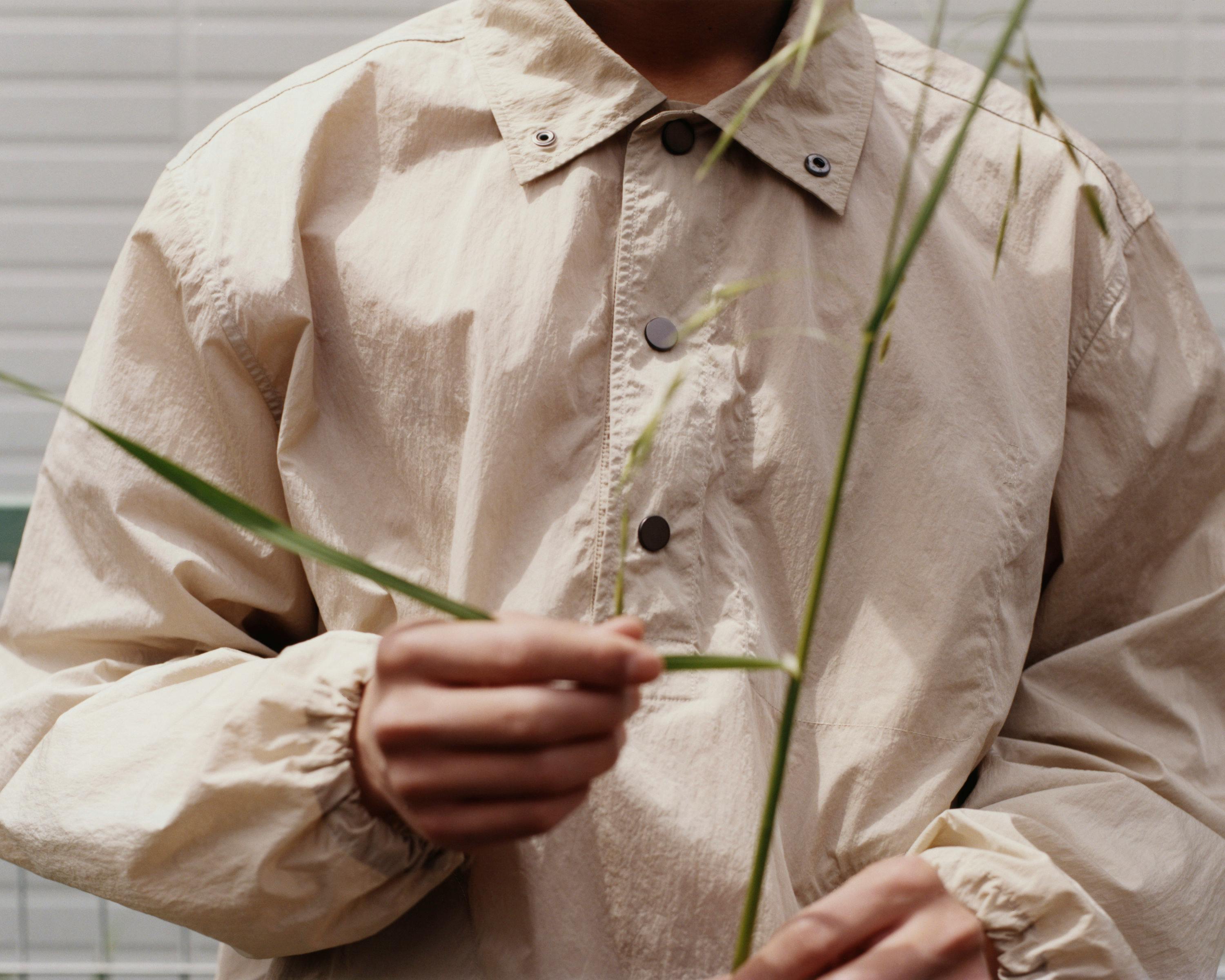 Close detail of a pale technical Morrow jacket held with field grass