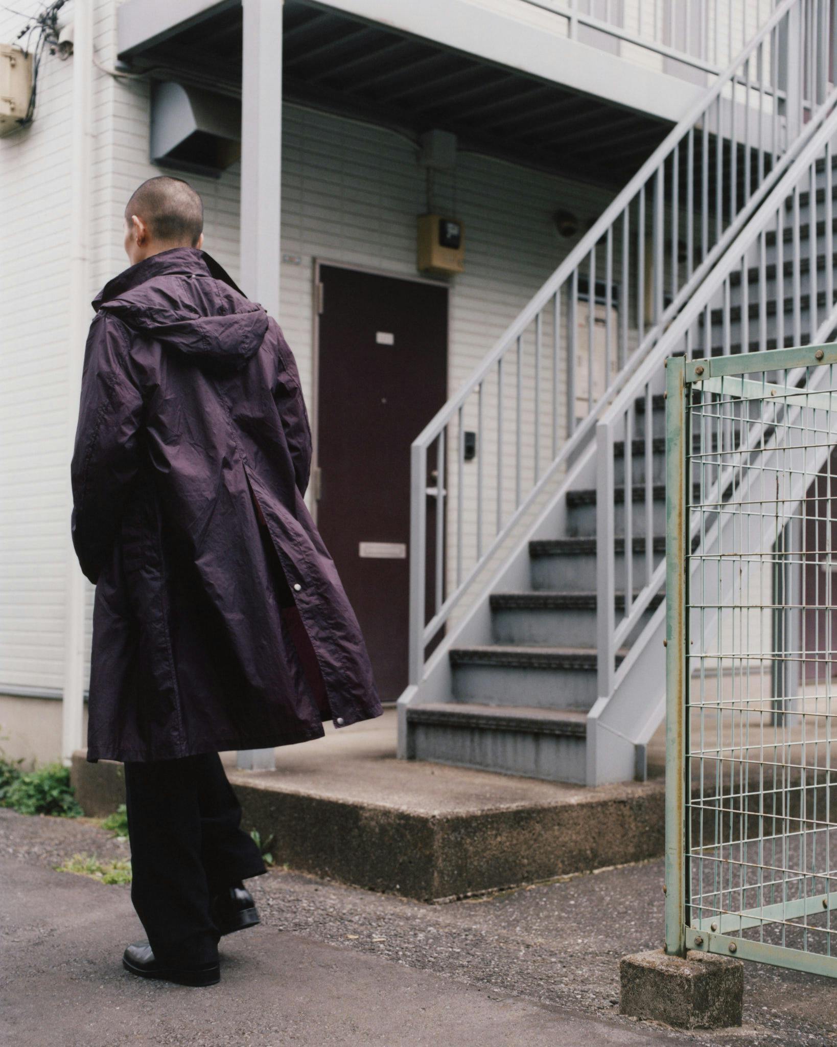 Rear view of a dark Morrow raincoat beside an exterior stairway