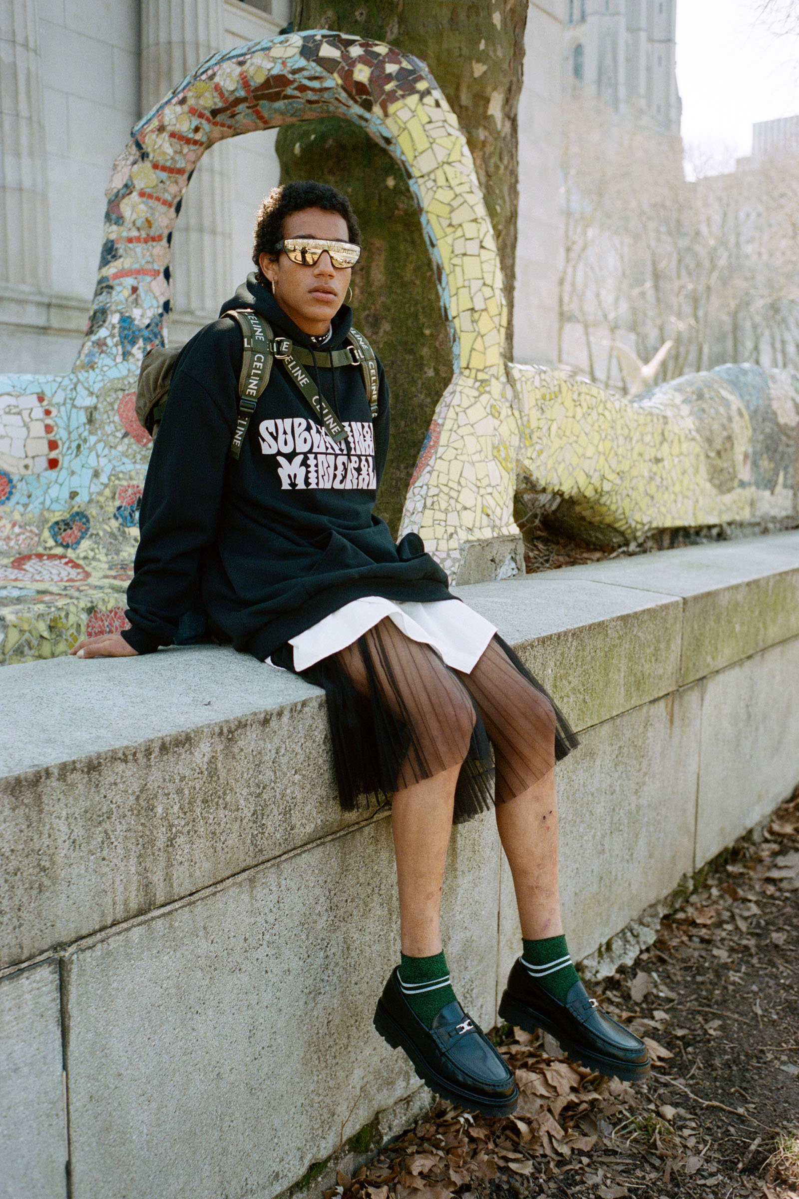 Top, skirt, hoodie, sunglasses, necklace, and shoes CELINE HOMME BY HEDI SLIMANE Trekking Backpack in Cotton Gabardine with Celine Print Khaki CELINE HOMME BY HEDI SLIMANE Earrings and socks MYLES’S OWN