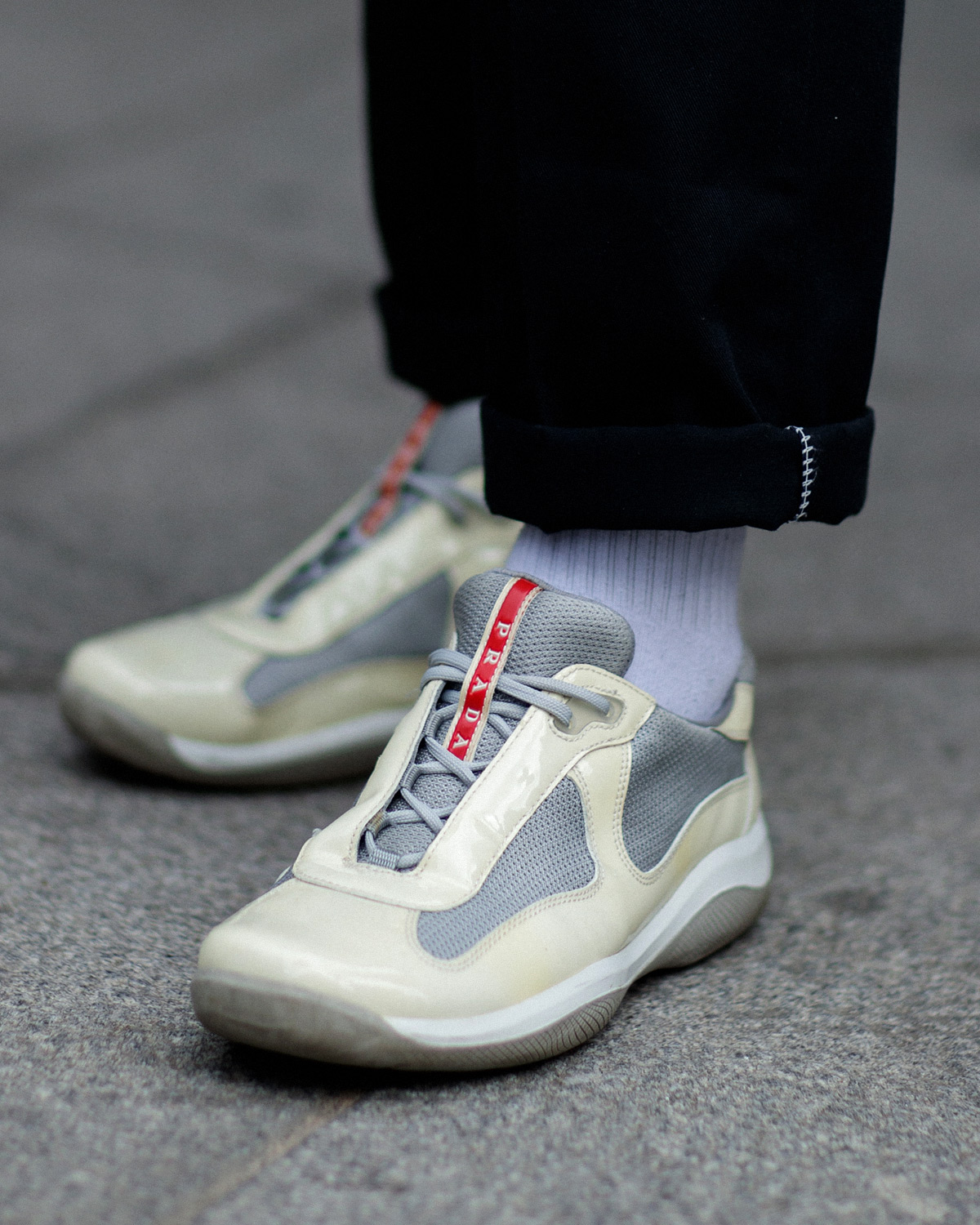 A person wearing Prada America’s Cup Original Sneakers in white with a grey and red detailing