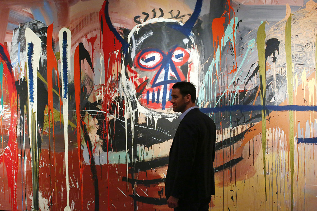 man stands next to the artwork 'Untitled' made by artist Jean-Michel Basquiat