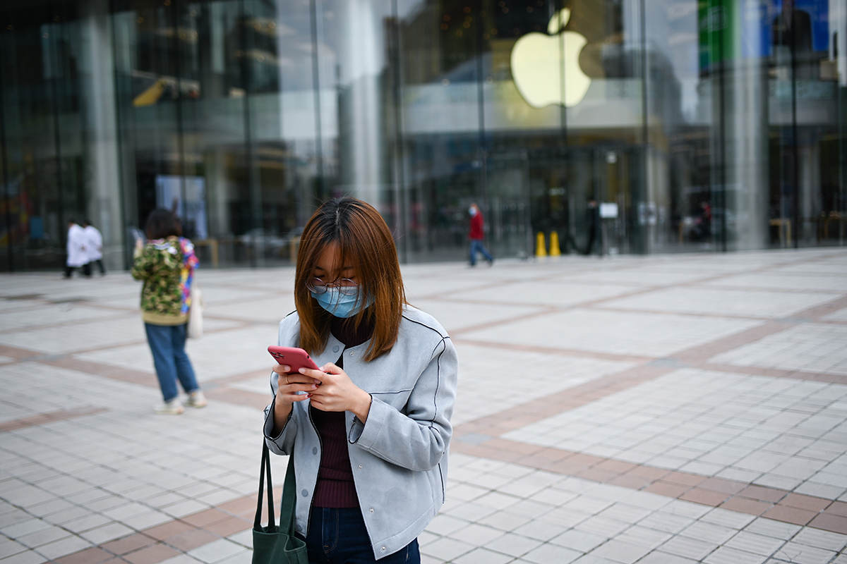 A woman wearing a face mask looks at her mobile phone outside an Apple Store in Beijing