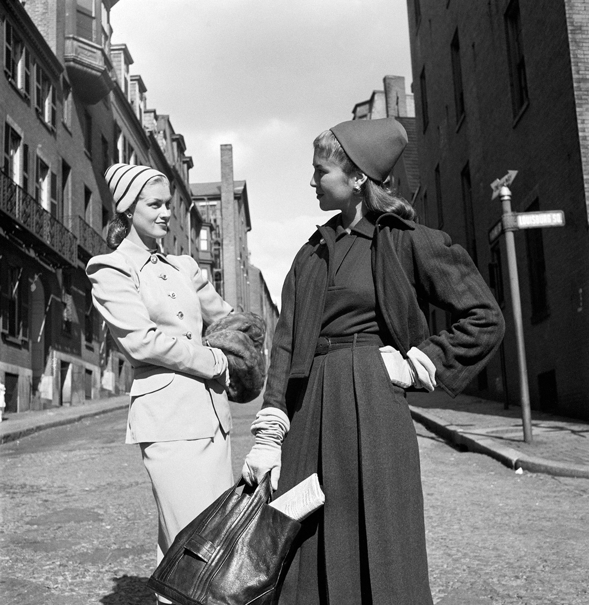 A woman models a herringbone tweed suit (left) by Clare McCardell while another model shows a juilliard gabardine wool suit by Eisenberg in Boston's Louisburg Square, 1946